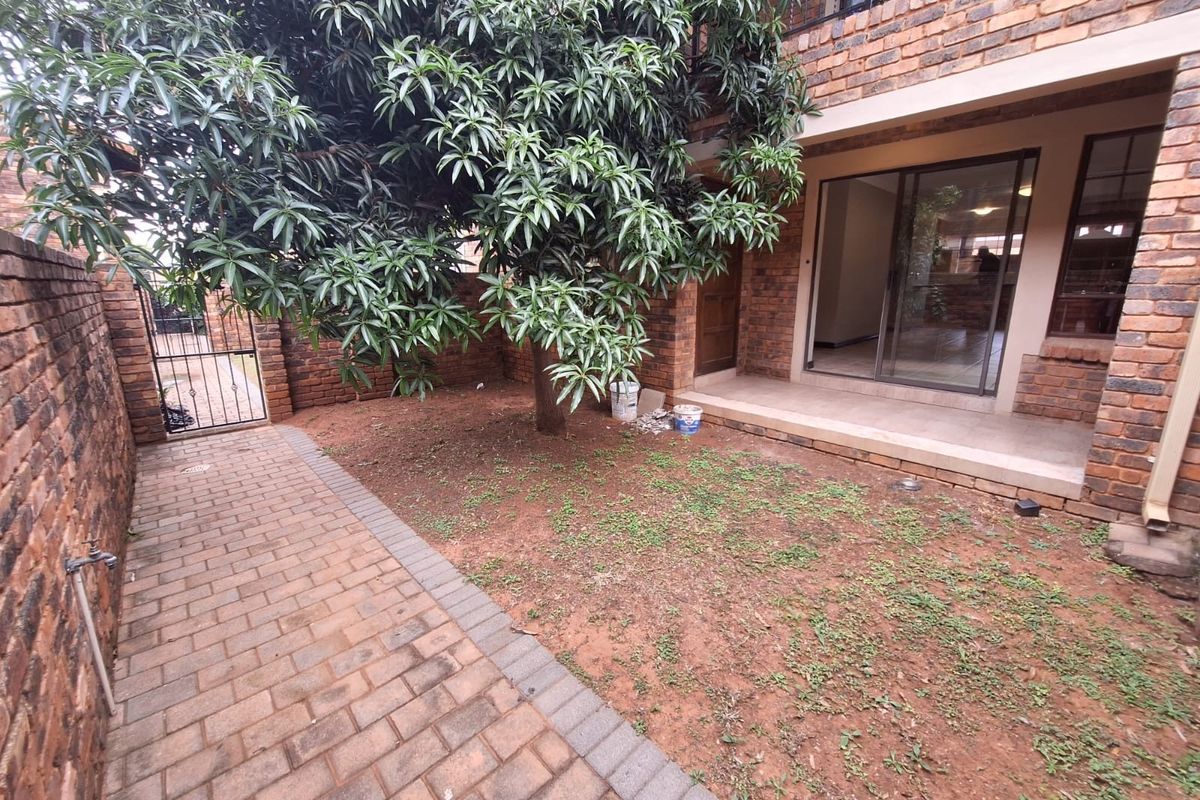 A private rear courtyard featuring brick paving, a covered patio area, and a mature tree, providing a functional outdoor space for the townhouse.