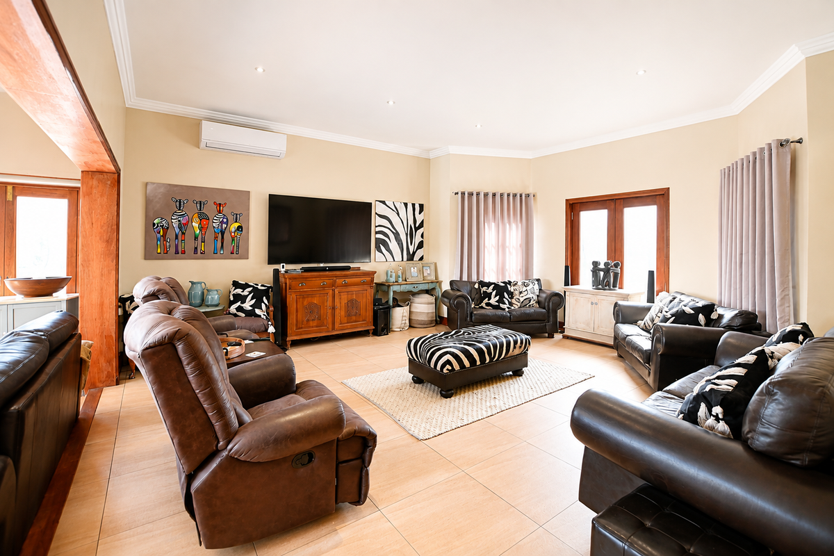 A spacious living room featuring tiled flooring, recessed downlighting, and a wall-mounted air conditioning unit, with direct access to outdoor areas via wooden doors.