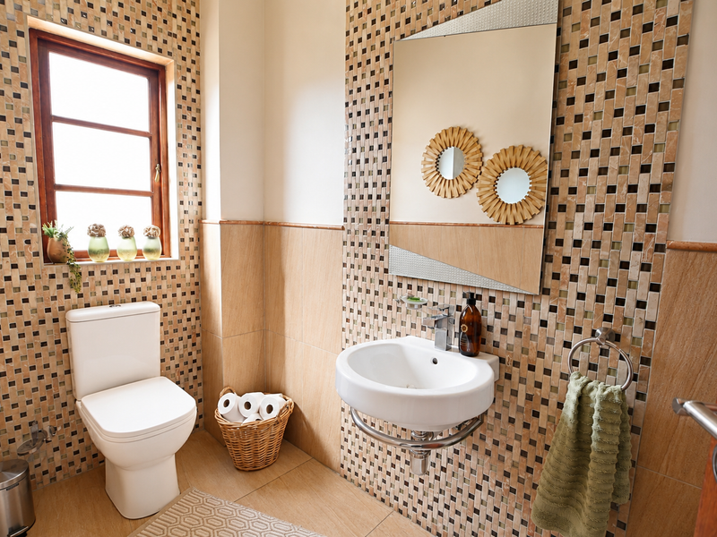 A well-maintained bathroom featuring mosaic wall tiling, a wall-mounted basin with chrome fixtures, and a close-coupled toilet with natural light from a timber window.