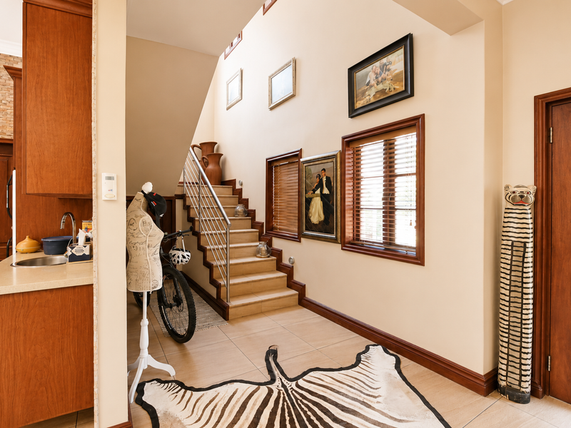 Spacious entrance hall featuring a tiled staircase with a modern stainless steel balustrade, adjacent to a functional kitchen area with wooden cabinetry.