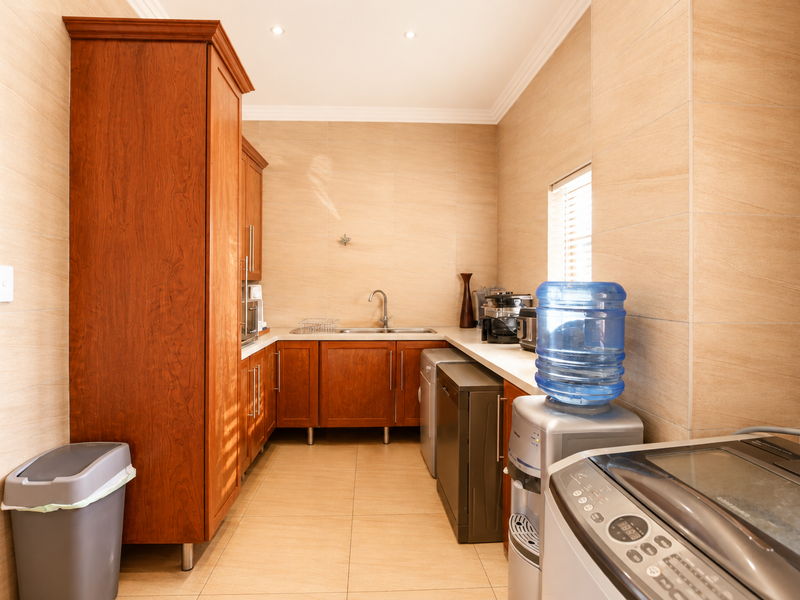 A functional laundry room featuring wood-finish cabinetry, tiled walls and flooring, and a stainless steel sink with integrated plumbing connections.