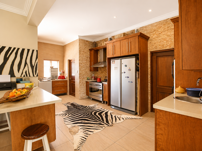 Spacious kitchen featuring warm wooden cabinetry, stone veneer wall accents, quartz countertops, and integrated stainless steel appliances with recessed lighting.