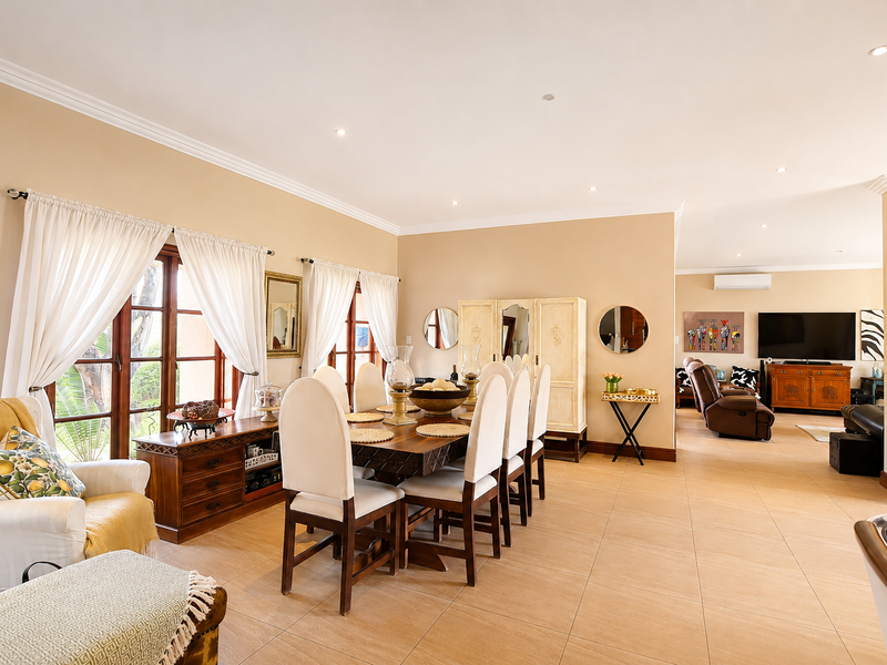 Spacious open-plan dining and living area featuring neutral walls, tiled flooring, recessed lighting, and large wooden-framed windows providing natural light.