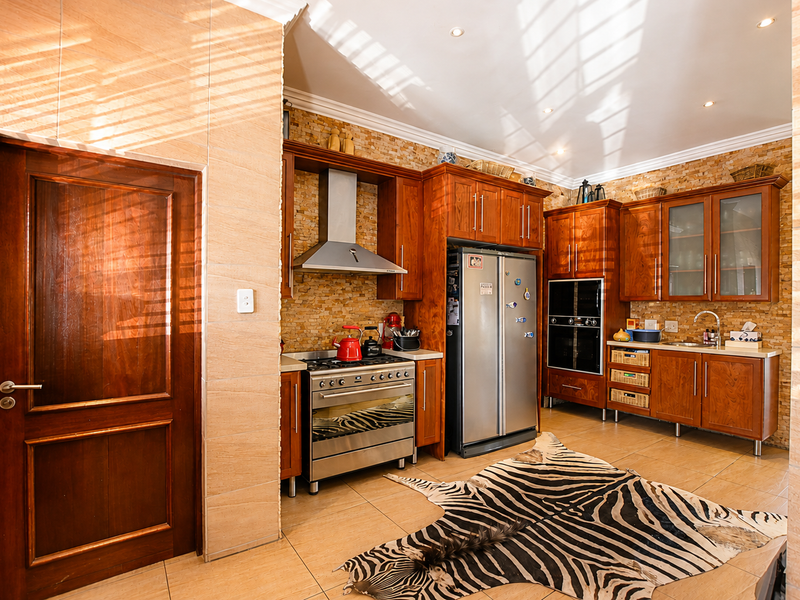 A well-equipped kitchen featuring warm-toned wooden cabinetry, stone tile backsplash, stainless steel appliances, and tiled flooring with recessed lighting.