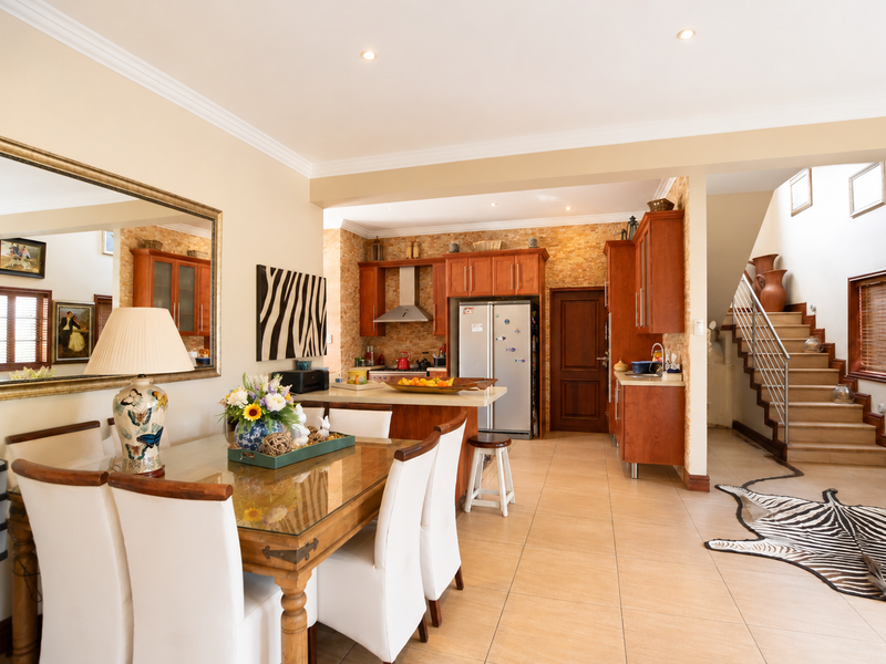 Spacious open-plan living and dining area featuring a well-appointed kitchen with wooden cabinetry, stone backsplash, and a staircase leading to the upper level.