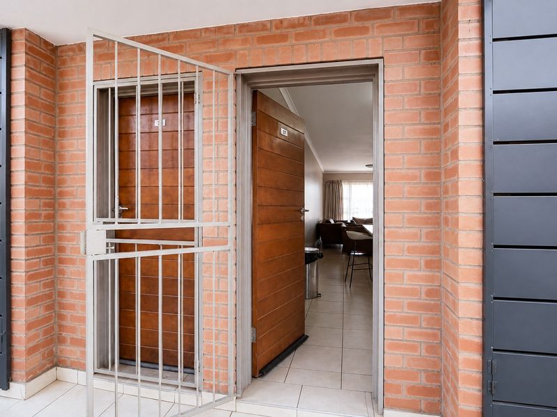 Apartment entrance featuring a secure metal gate, solid timber door, and exposed brick exterior wall finish.
