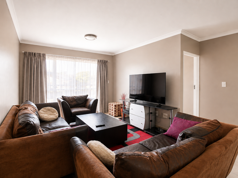 A well-maintained living room featuring neutral wall tones, tiled flooring, and large windows with natural light, providing a comfortable and functional living space.