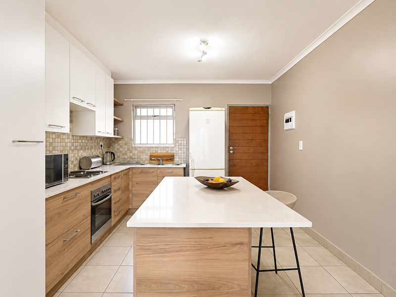 Modern kitchen featuring wood-finish cabinetry, a central island with stone countertop, built-in oven, hob, and tiled flooring.