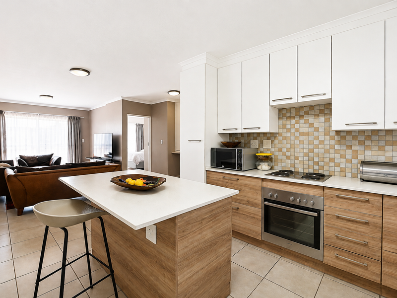 Open-plan living area featuring a modern kitchen with wood-finish cabinetry, stone countertops, built-in oven, and a central island, flowing into a spacious lounge.