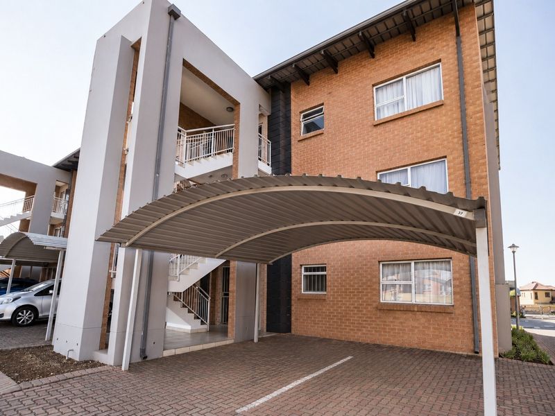 Exterior view of a modern apartment complex featuring brick facade, covered parking bays, and external staircases providing access to upper-level units.