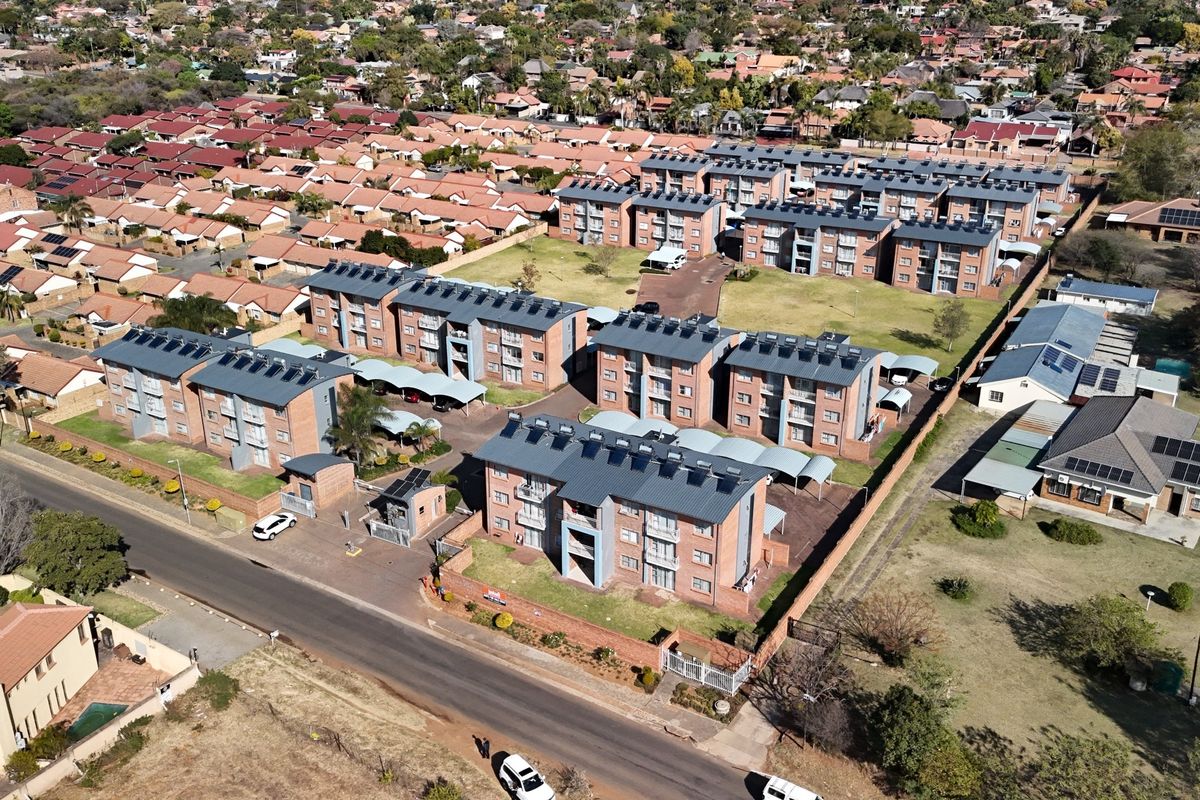 Aerial view of a residential apartment complex featuring multiple brick buildings, solar water heating systems, paved parking areas, and secure gated access.
