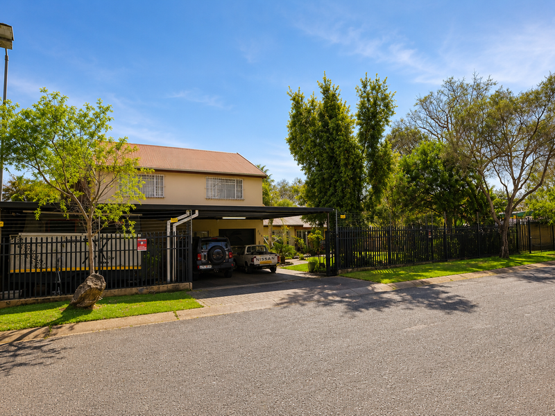 Front exterior view of the property featuring a paved driveway, metal carport, and secure perimeter fencing with security bars on windows.