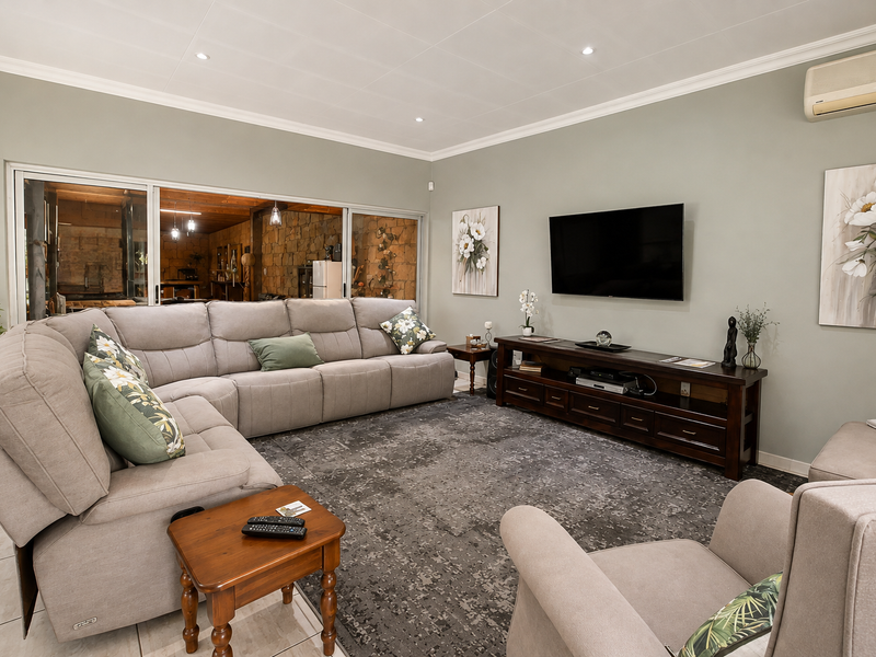 A comfortable living room featuring tiled flooring, recessed downlighting, coved cornicing, and large sliding glass doors that provide a view into the adjacent space.