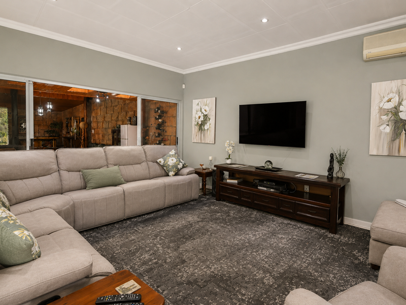 A comfortable living room featuring recessed lighting, crown molding, and a wall-mounted air conditioning unit, with sliding glass doors opening to an outdoor area.
