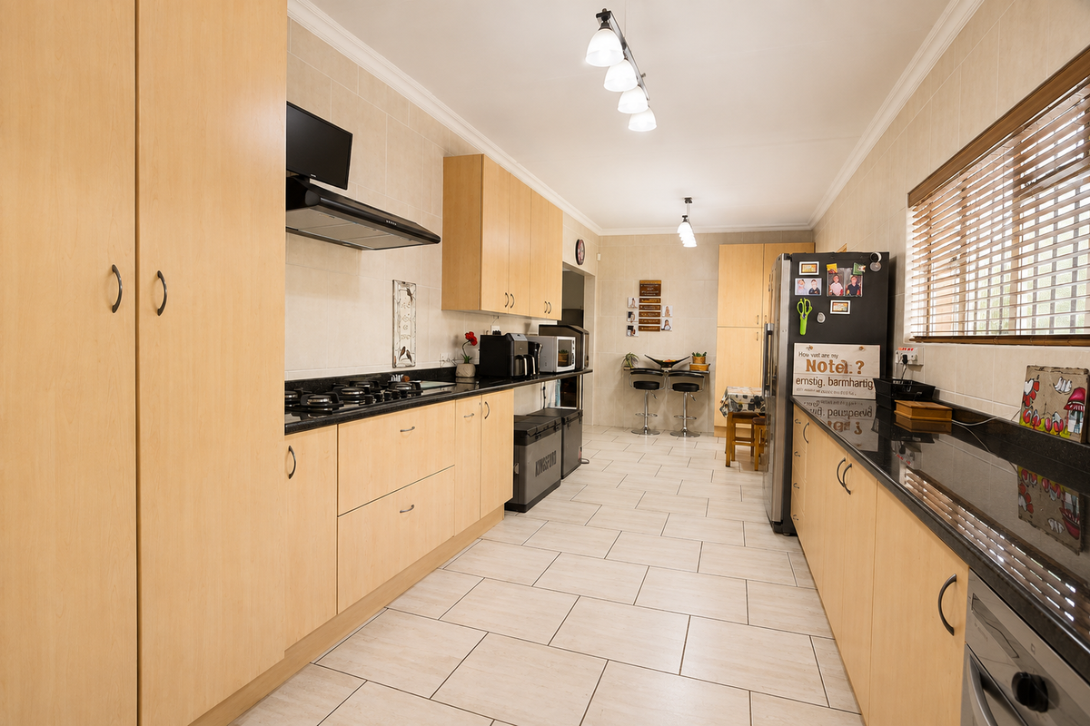 A well-maintained kitchen featuring light wood cabinetry, granite countertops, a gas hob with extractor, and tiled flooring throughout.