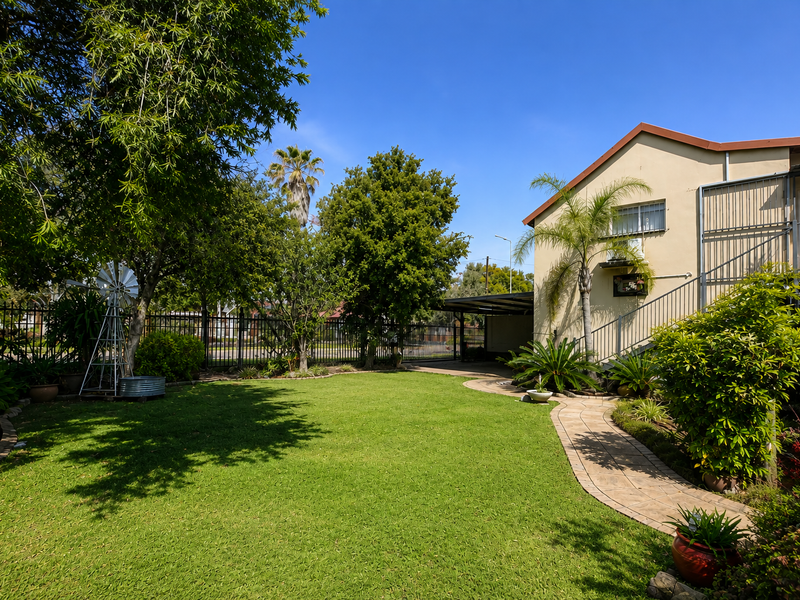 A well-maintained garden featuring a lush lawn, paved walkway, and secure perimeter fencing with a metal staircase leading to the upper level.