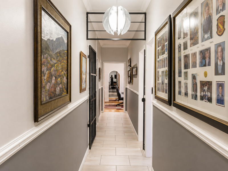 A well-maintained hallway featuring tiled flooring, wainscoting, and a decorative ceiling light fixture, leading through a security gate to an adjacent room.