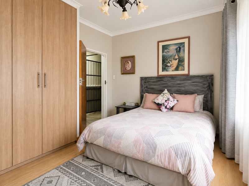 A well-maintained bedroom featuring light wood-look laminate flooring, a large built-in wardrobe, and neutral wall finishes.