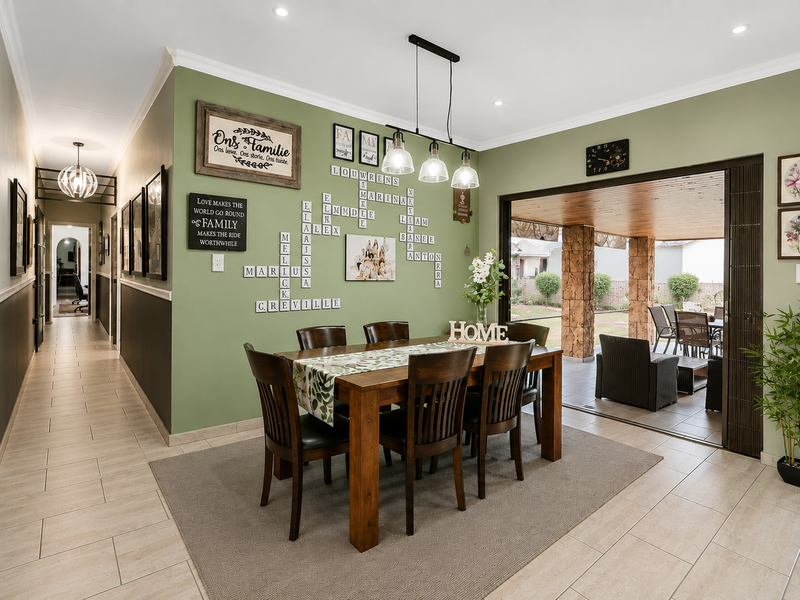 A well-maintained dining room featuring tiled floors, modern pendant lighting, and large stacking doors that open onto a covered patio area.