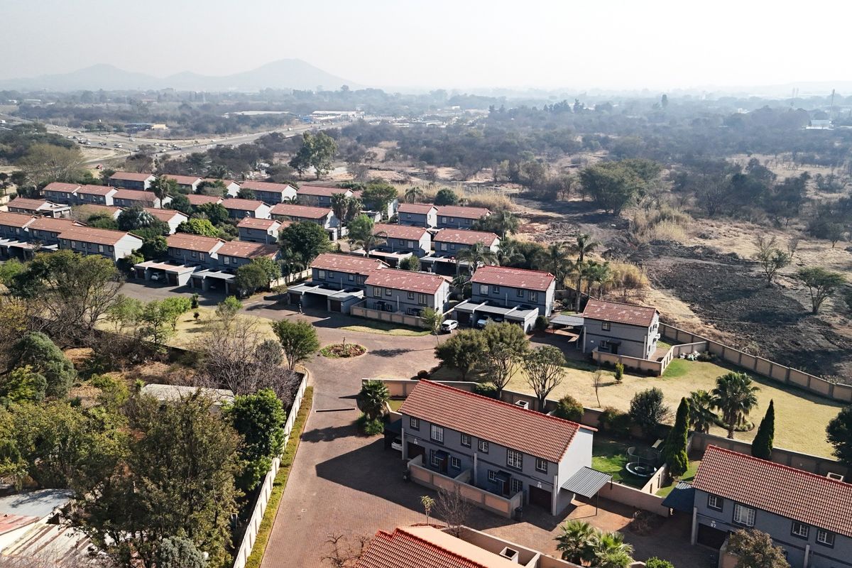 Aerial view of a residential townhouse complex featuring multiple units with tiled roofs, paved driveways, and established garden areas.