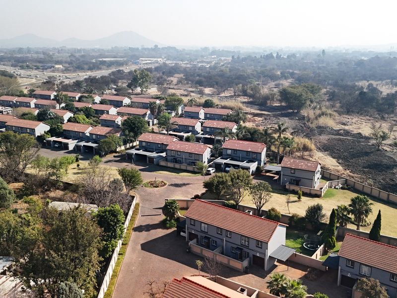Aerial view of a residential townhouse complex featuring multiple units with tiled roofs, paved driveways, and established garden areas.