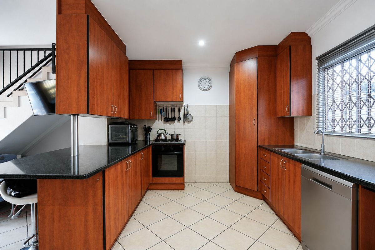 A functional kitchen featuring warm-toned built-in cabinetry, granite countertops, a built-in oven, and tiled flooring, with a window fitted with a security gate.