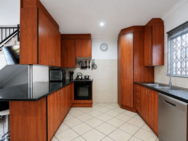A functional kitchen featuring warm-toned built-in cabinetry, granite countertops, a built-in oven, and tiled flooring, with a window fitted with a security gate.