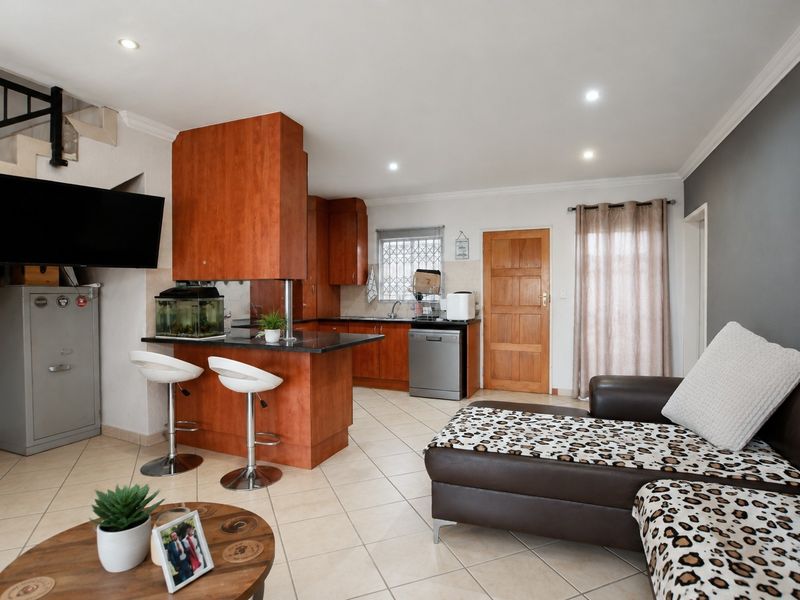 Open-plan living and kitchen area featuring tiled floors, wooden cabinetry, granite countertops, and a staircase leading to the upper level.