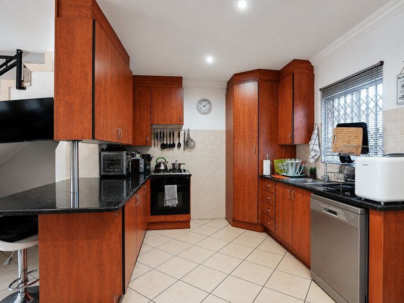 Functional kitchen featuring warm-toned built-in cabinetry, granite countertops, tiled backsplash, and integrated appliances, with adjacent staircase access.