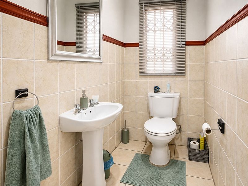 A clean and functional guest bathroom featuring a pedestal basin, toilet, and neutral ceramic wall and floor tiling with a decorative wooden dado rail.