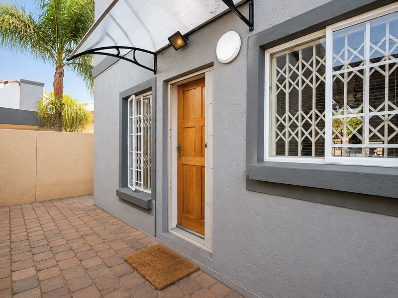 A well-maintained rear exterior area featuring a paved patio, secure entrance door with security gate, and a protective awning over the doorway.
