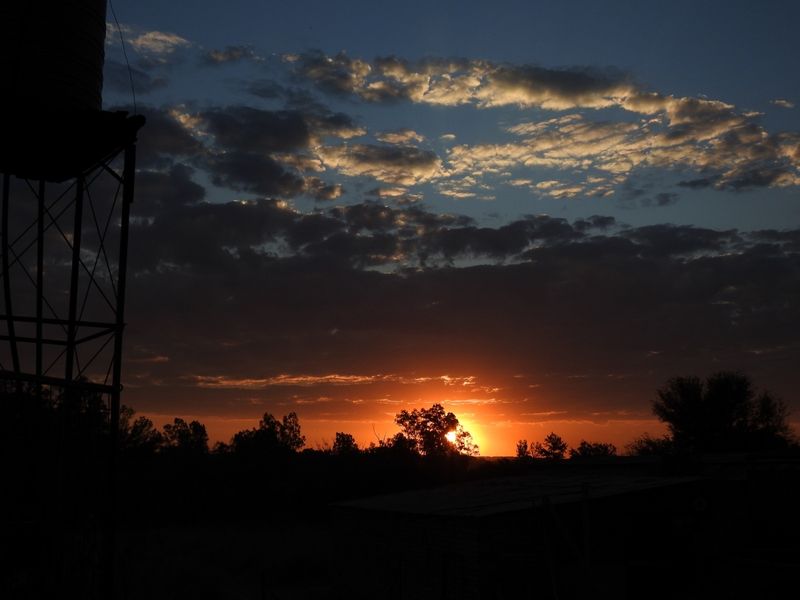 A scenic sunset view over the small holding landscape, featuring a silhouette of a water tank stand against the evening sky.