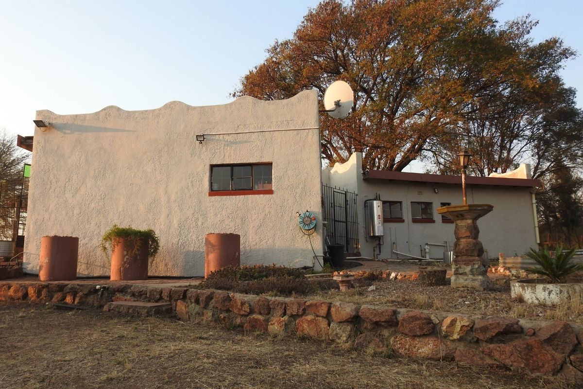 Rear exterior view of the property featuring a scalloped parapet wall, stone retaining wall, and established garden surroundings.