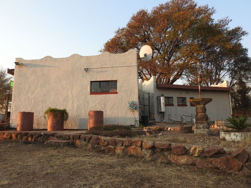 Rear exterior view of the property featuring a scalloped parapet wall, stone retaining wall, and established garden surroundings.