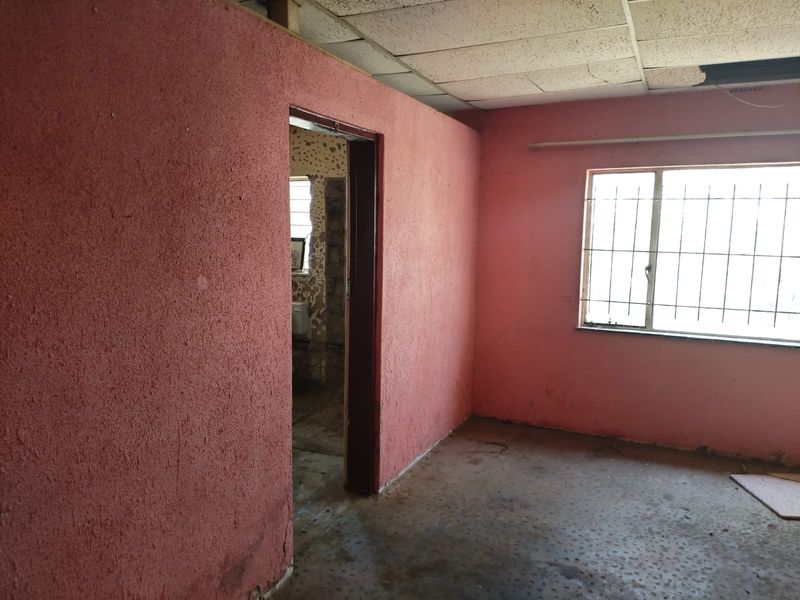 An empty bedroom featuring textured pink walls, security bars on the window, and a drop ceiling in need of repair.