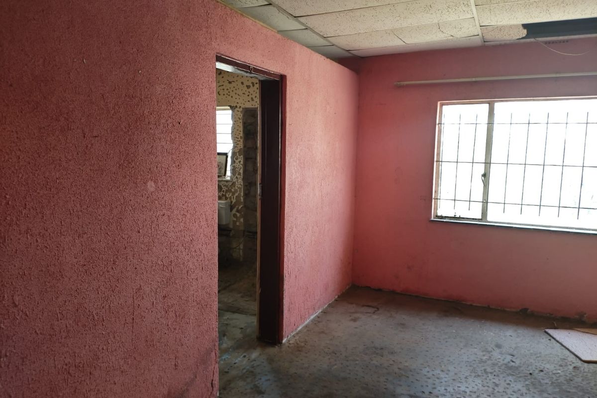 An empty bedroom featuring textured pink walls, security bars on the window, and a drop ceiling in need of repair.