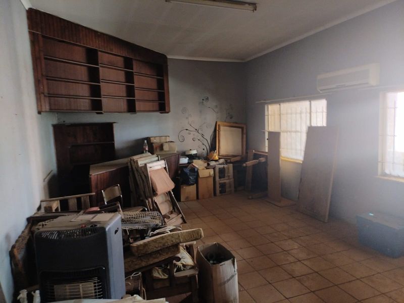 A spacious living area featuring built-in wooden shelving, tiled flooring, and a wall-mounted air conditioning unit, currently used for storage.