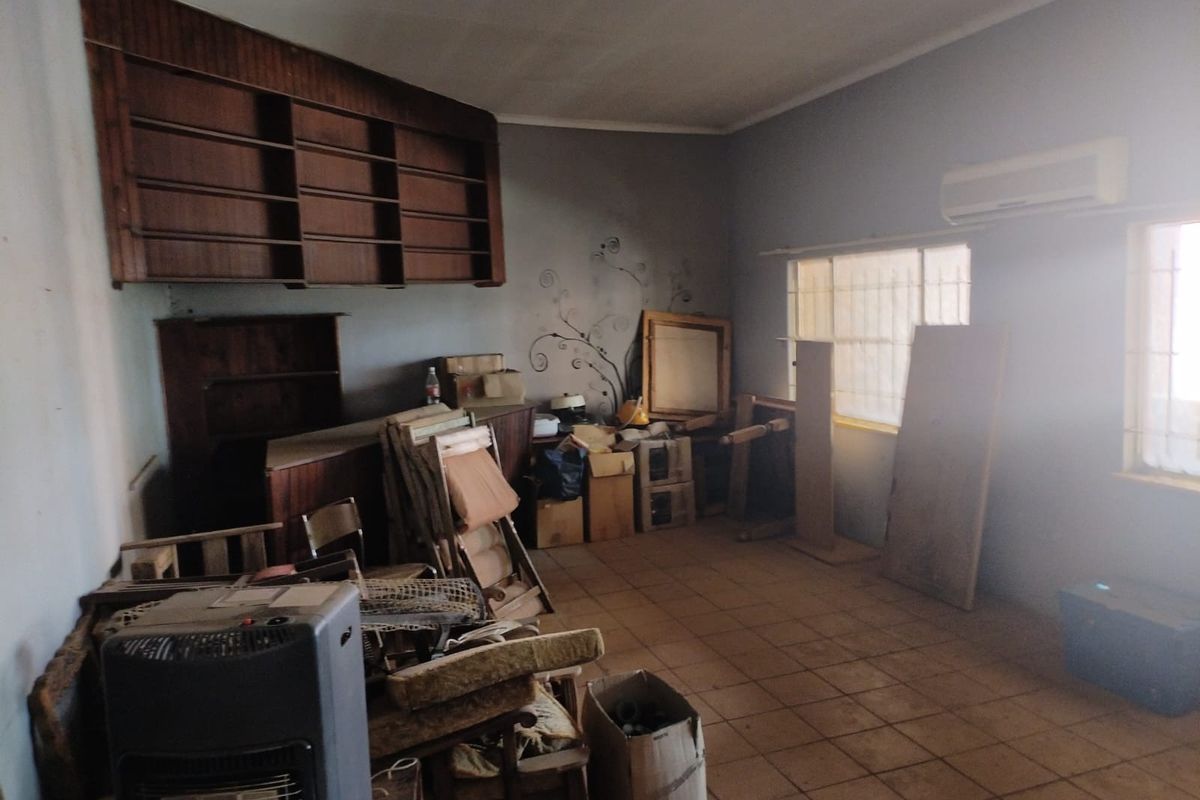 A spacious living area featuring built-in wooden shelving, tiled flooring, and a wall-mounted air conditioning unit, currently used for storage.