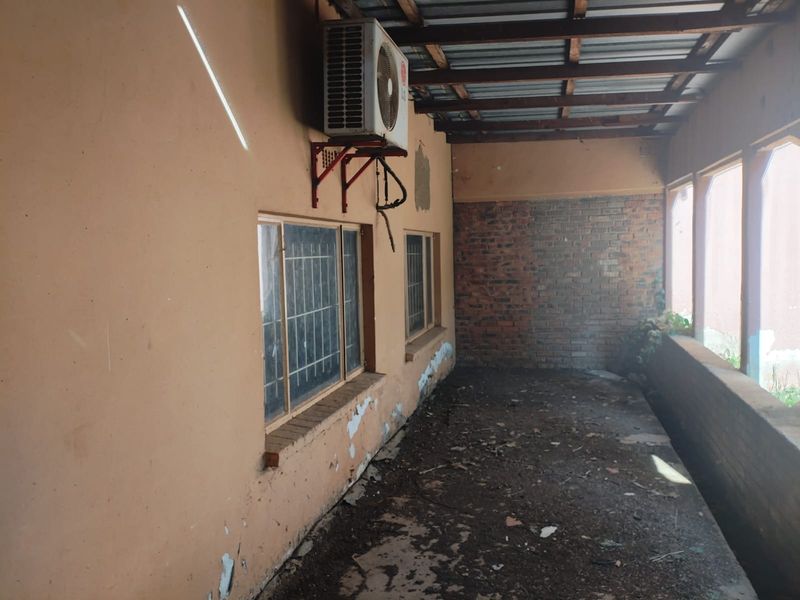 A covered outdoor patio area featuring exposed brickwork, a metal roof structure, and wall-mounted air conditioning unit, requiring maintenance and cosmetic repairs.
