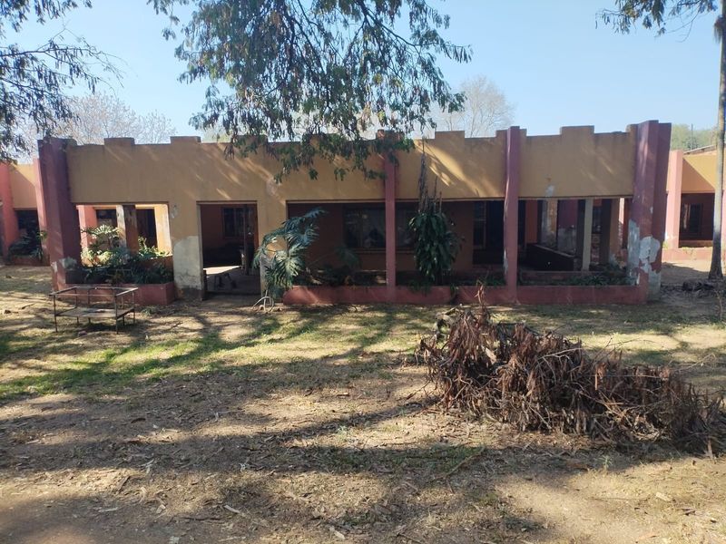 Rear view of a small holding dwelling featuring a covered patio area with masonry pillars, showing significant signs of exterior wear and maintenance requirements.