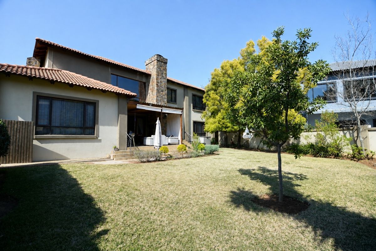 Rear view of the house featuring a spacious lawn, landscaped garden, stone chimney, and a covered patio area.
