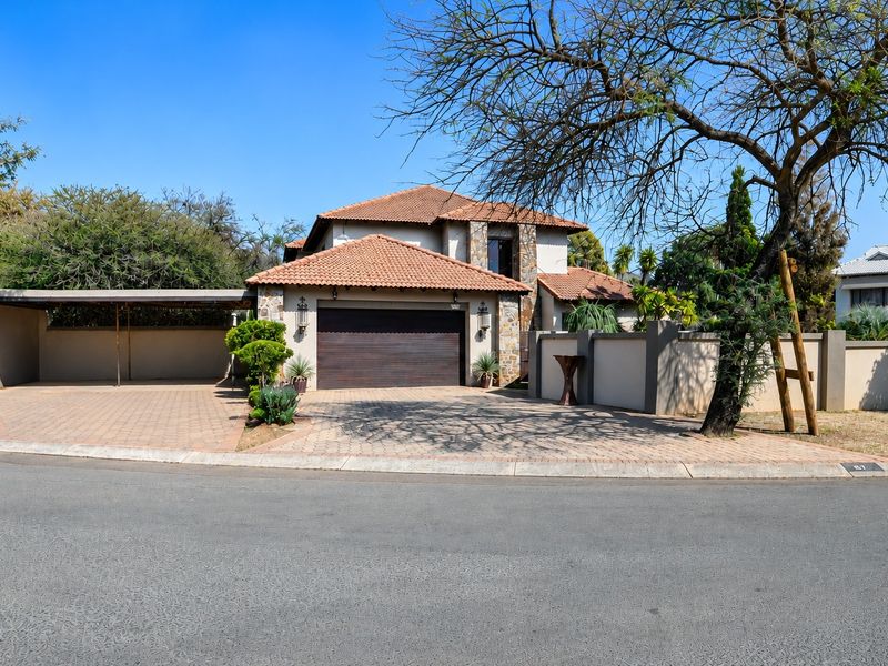 Front elevation of a well-maintained house featuring a tiled roof, stone accents, a double garage, and a paved driveway with an attached carport.