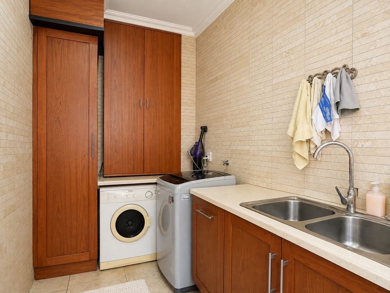 A functional laundry room featuring built-in wooden cabinetry, a double stainless steel sink, and tiled wall finishes.