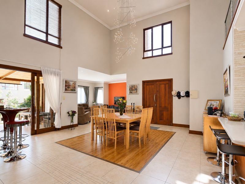 Spacious open-plan living and dining area featuring double-volume ceilings, large windows, tiled floors with wood inlay, and seamless access to the outdoor patio.