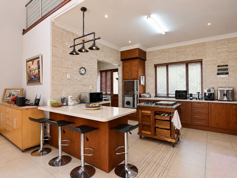 A spacious kitchen featuring warm wood cabinetry, stone countertops, a central island, and integrated appliances, complemented by neutral tiled flooring and recessed lighting.