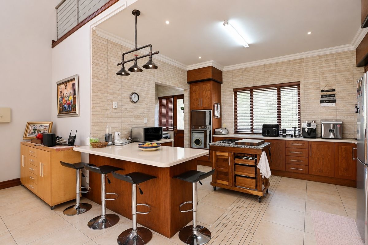 A spacious kitchen featuring warm wood cabinetry, stone countertops, a central island, and integrated appliances, complemented by neutral tiled flooring and recessed lighting.