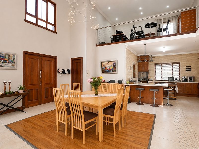 Spacious open-plan living and dining area featuring a mezzanine level, high ceilings, modern kitchen with island, and a blend of tiled and timber flooring.
