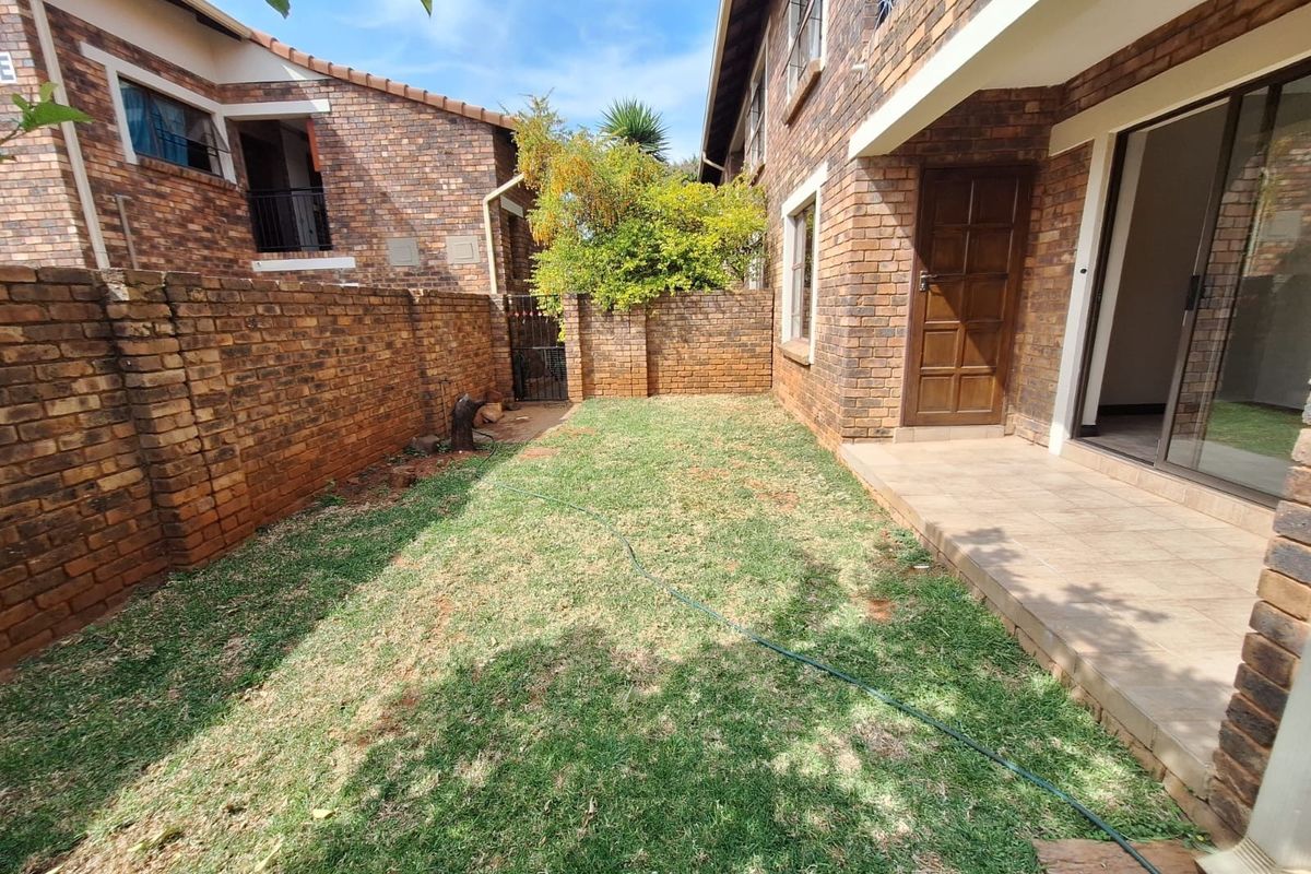 A private rear garden area featuring a small lawn, face brick boundary walls, and a tiled patio with sliding door access to the townhouse.