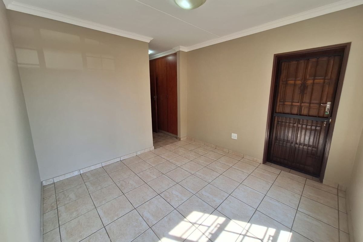 An empty living area featuring neutral wall paint, tiled flooring, and a secure wooden entrance door with a security gate.
