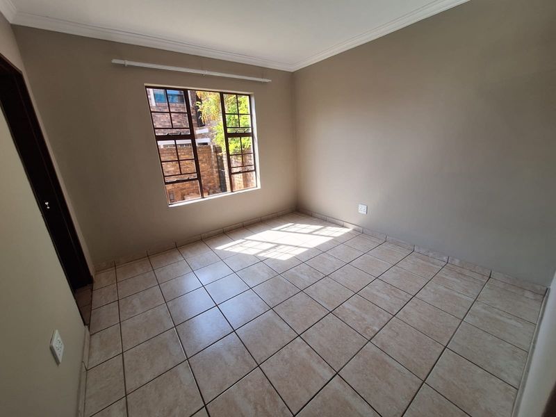 A bright, empty bedroom featuring neutral wall paint, tiled flooring, and a window fitted with security bars.